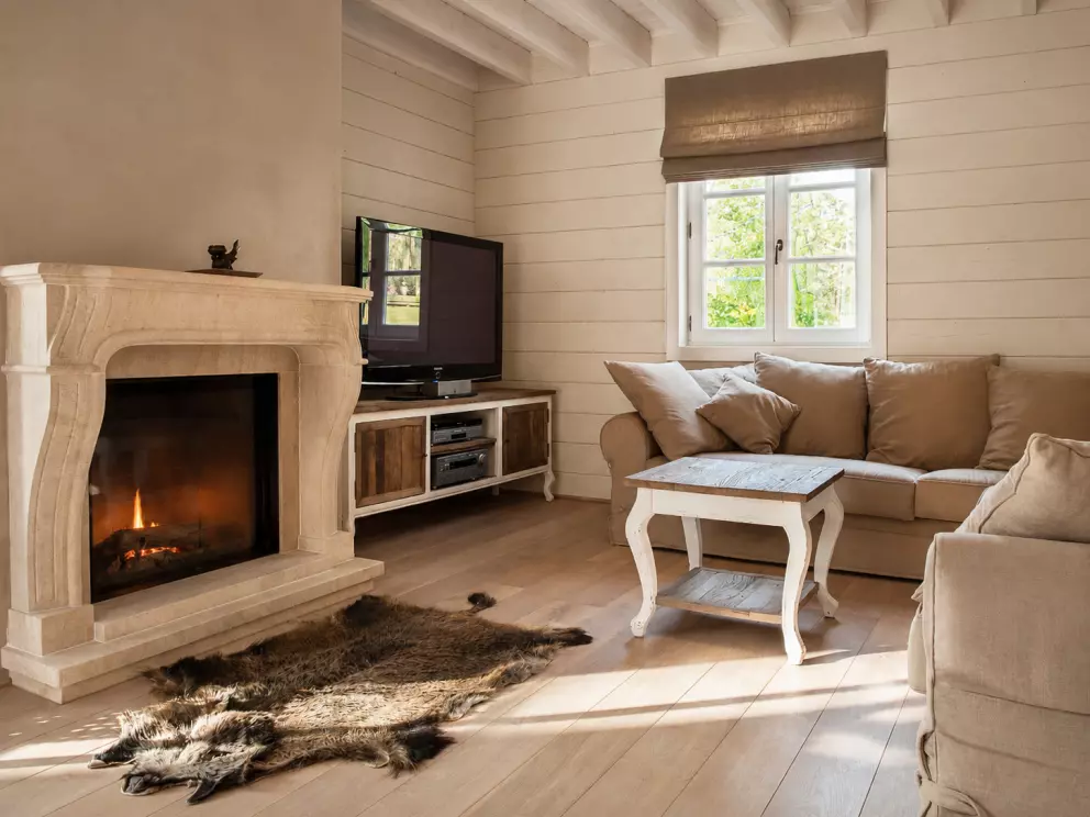 Rustige leefruimte in houtmassieve woning met lichte houten balken, haard en natuurlijk daglicht